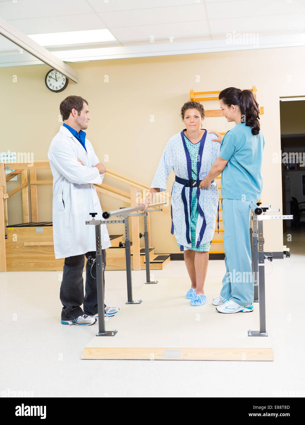 Physical Therapists Assisting Female Patient In Walking Stock Photo