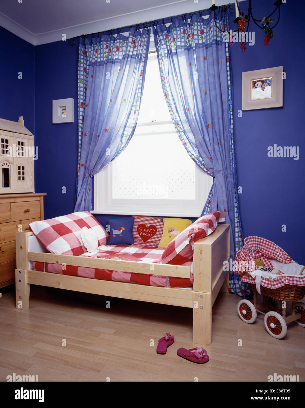 Blue Voile Drapes On Window Above Small Wooden Bed With Red White