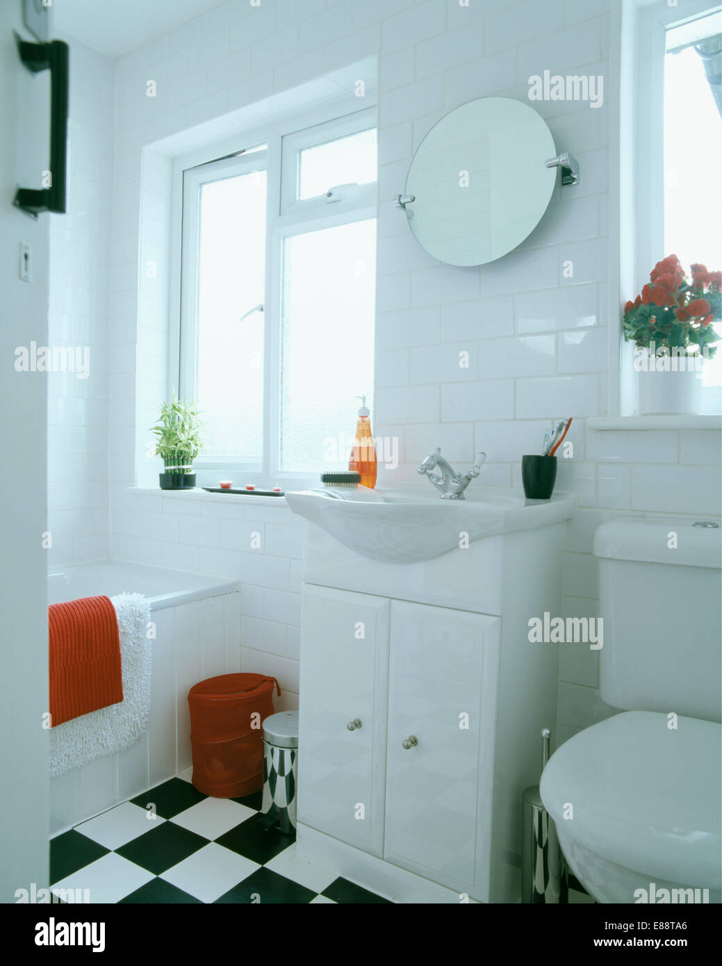 Circular mirror above basin in fitted vanity unit with small cupboard