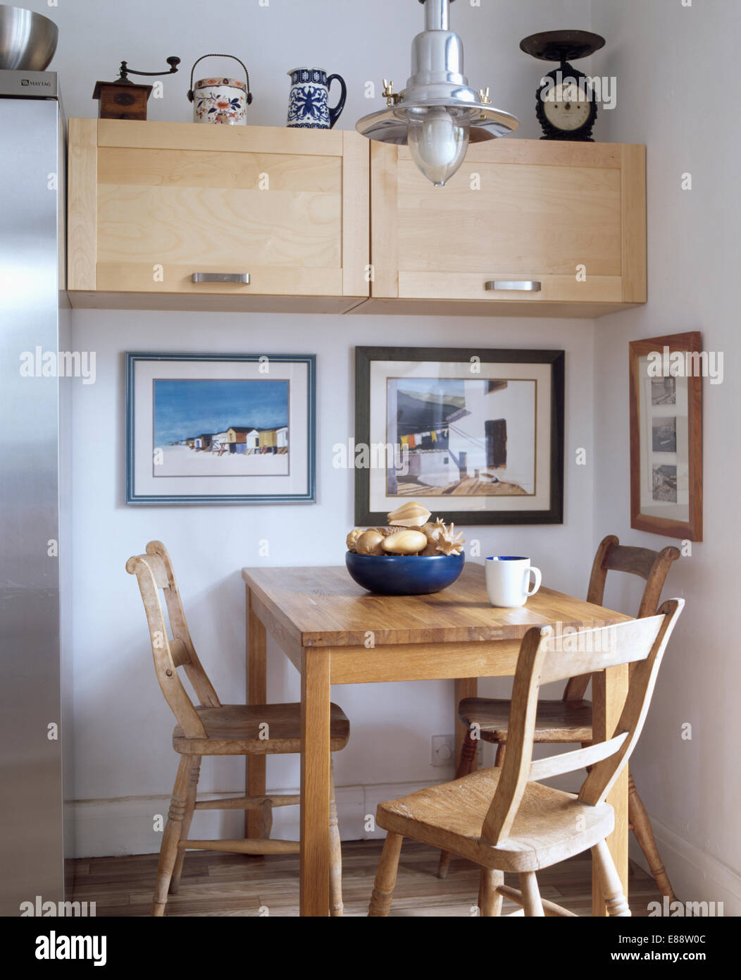 Small pale wood fitted cupboard and pictures on wall in dining area with  plain wood table and chairs Stock Photo - Alamy