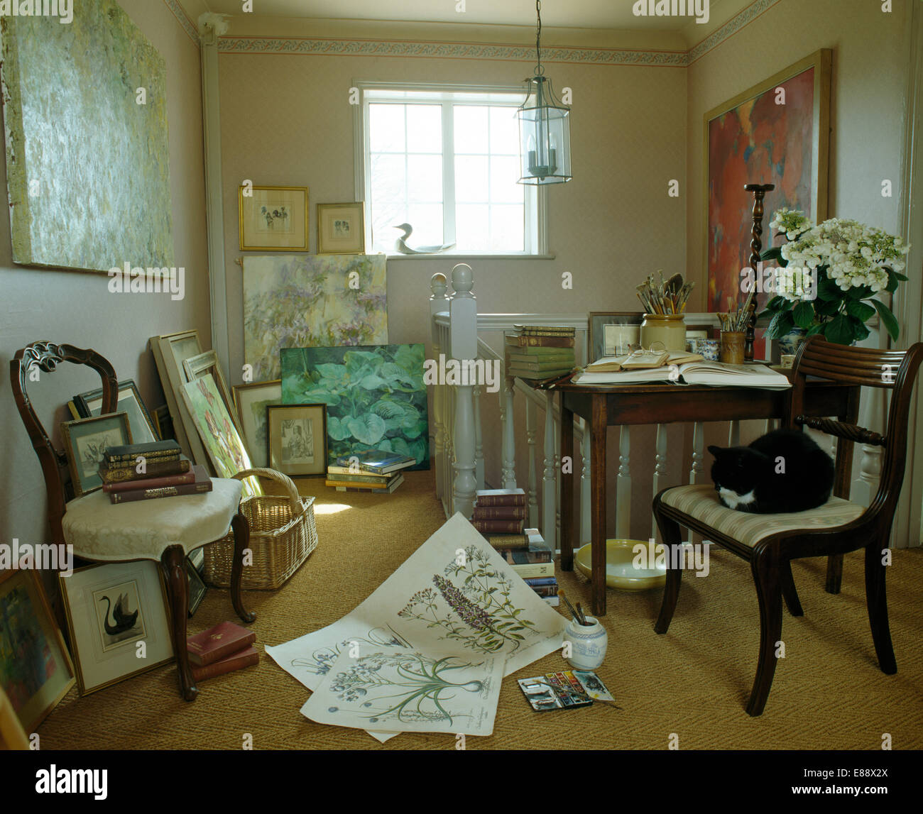 Antique chairs and paintings stacked against walls of landing studio with black cat sitting on chair Stock Photo