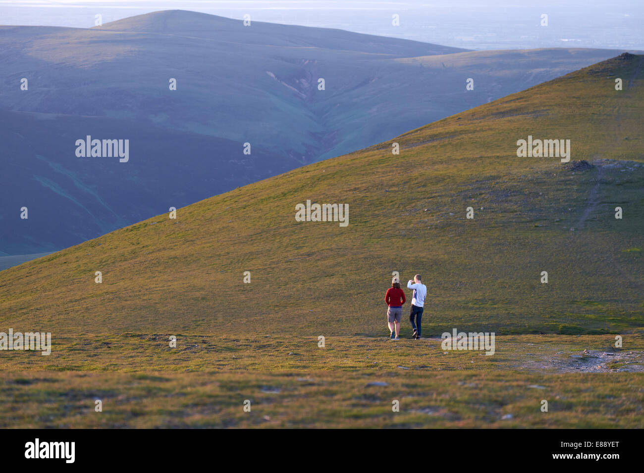 Two hikers exploring the summit of Blencathra at sunset in the Lake District, Cumbria, England.UK. Stock Photo