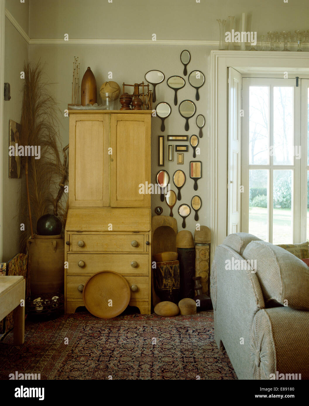 Collection of vintage hand mirrors on wall beside pine bureau in