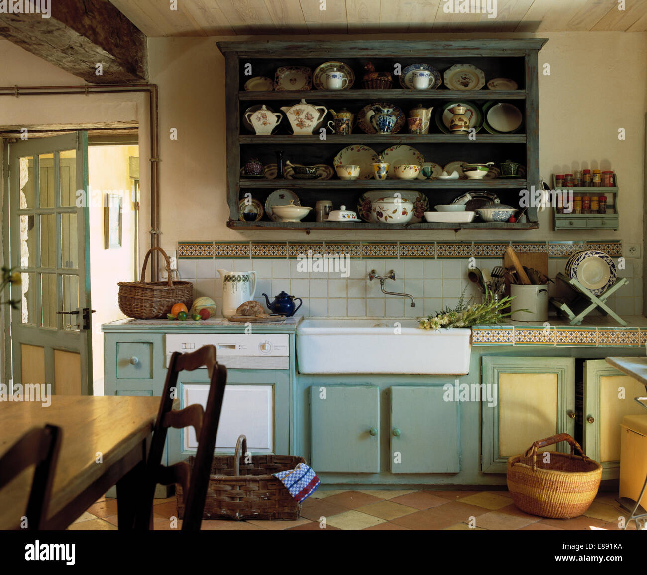 Dark green painted wooden shelves above large porcelain sink in green-blue fitted unit in country kitchen Stock Photo