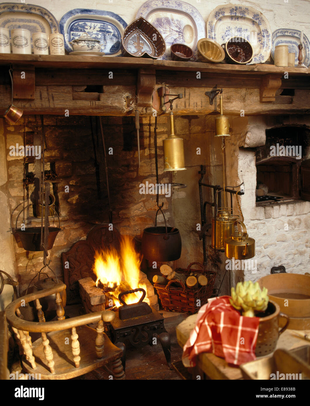 Wooden chair beside inglenook fireplace with lighted fire and row of meat plates on shelf Stock
