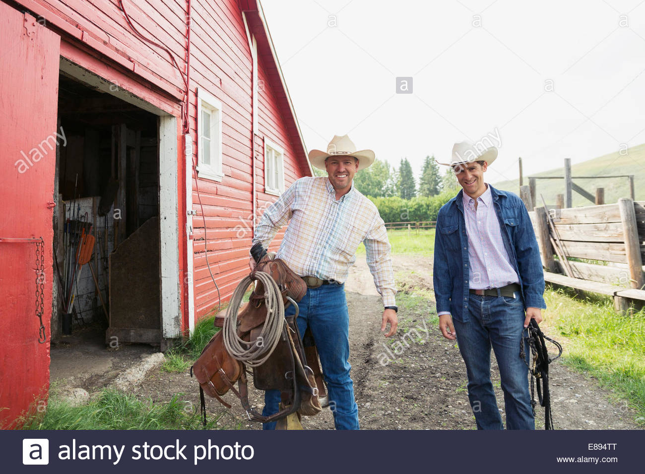 Ranchers carrying saddle and tack outside barn Stock Photo Alamy
