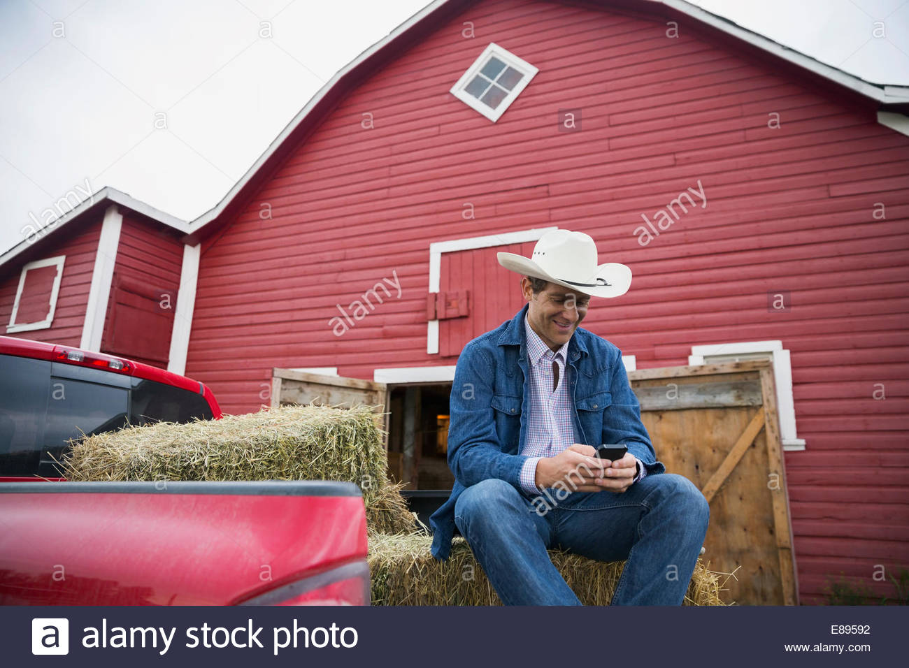 Rancher text messaging with cell phone outside barn Stock Photo