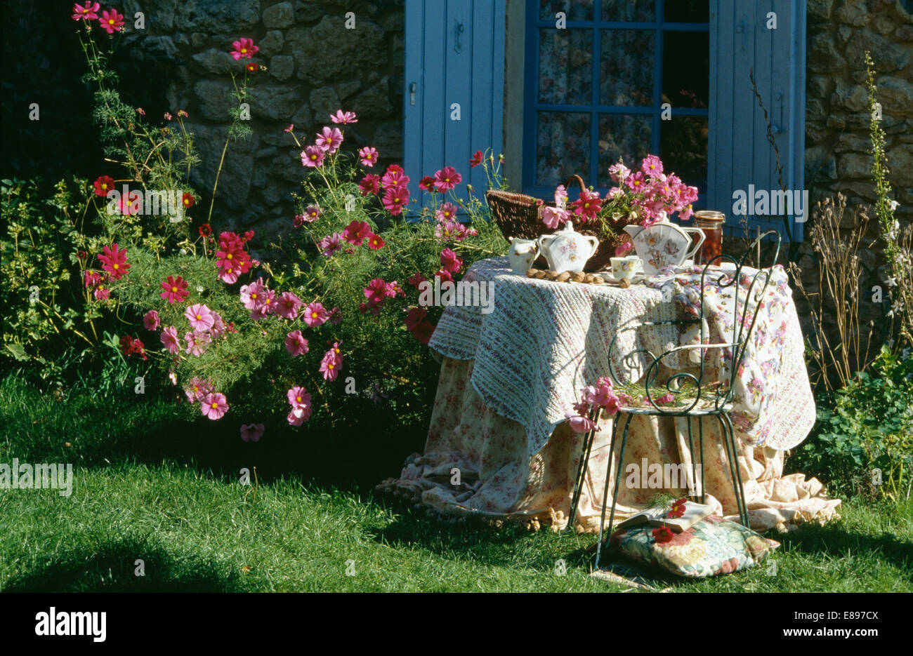 Vintage quilts on table in front of pink cosmos and window with blue shutters Stock Photo
