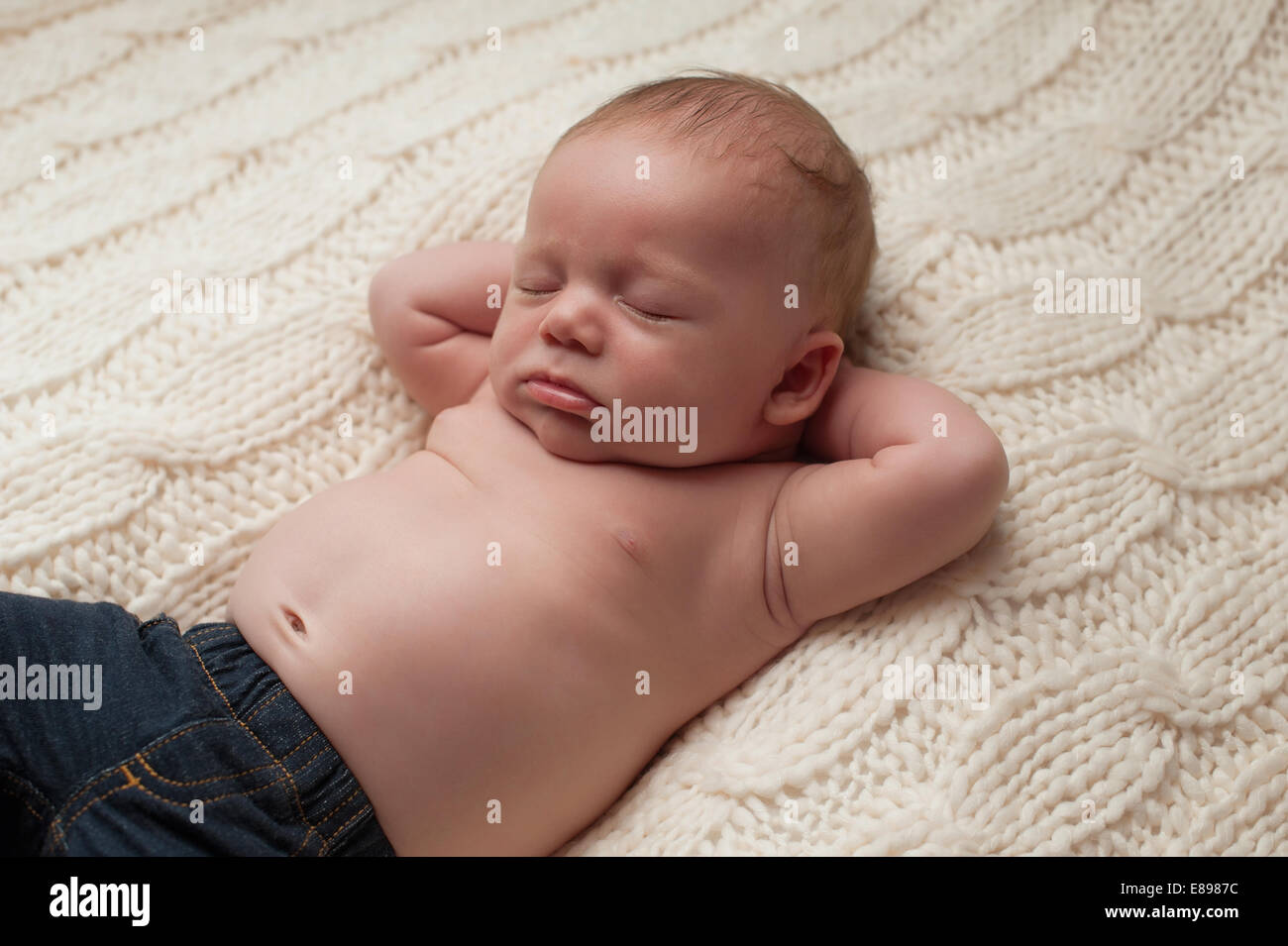 Portrait of a 1 month old newborn baby boy wearing jeans. He is sleeping on  his back a beige blanket with his hands behind his h Stock Photo - Alamy