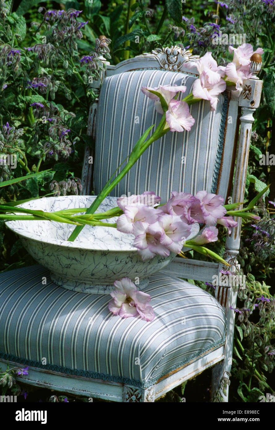 Still-Life of mauve gladioli in bowl on blue+white striped upholstered chair Stock Photo
