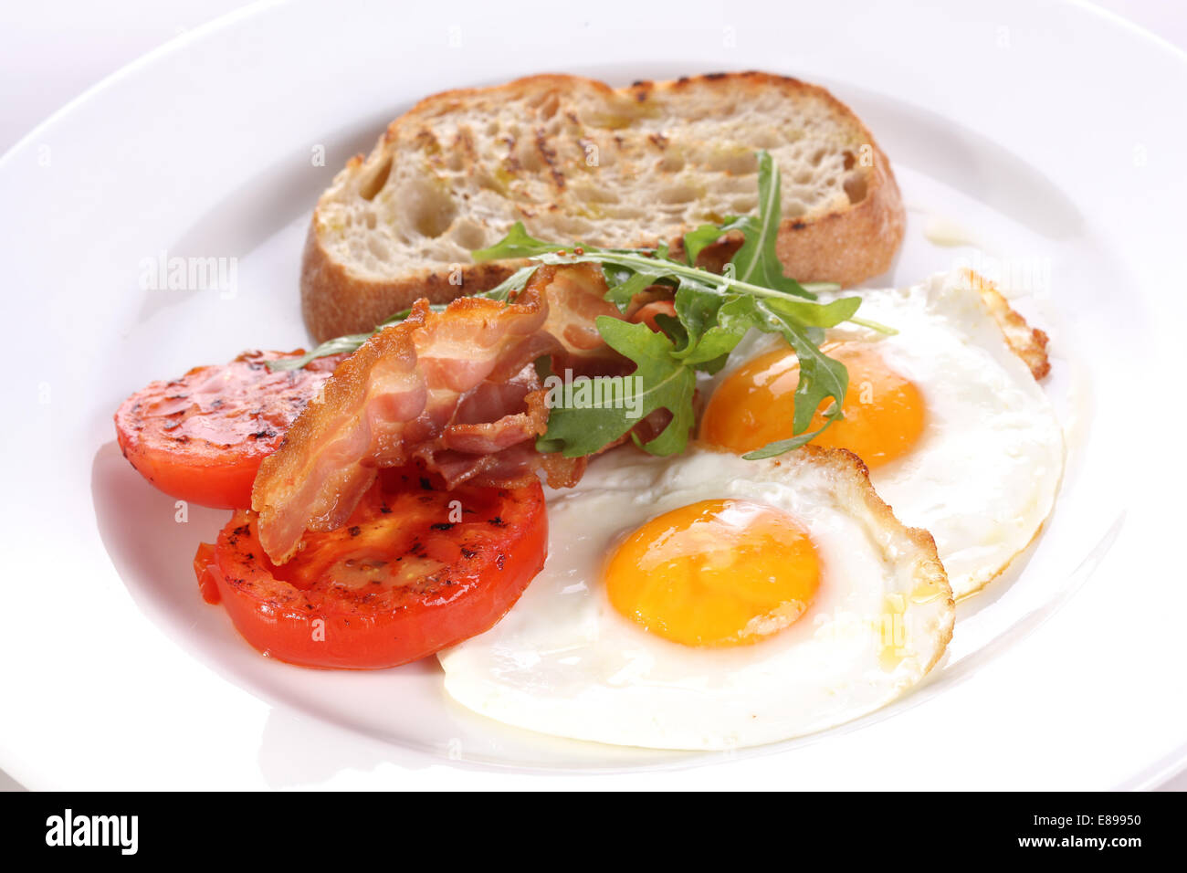 Freid eggs with tomatoes and becon on a white plate. Stock Photo