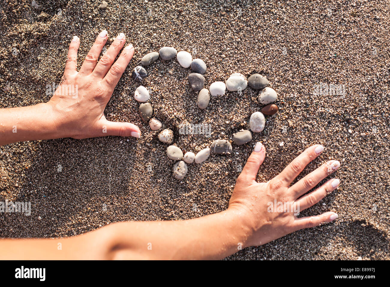 Woman's hands making heart of marine shingles on the sand. Stock Photo