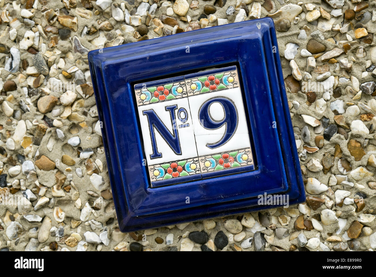 The number 9 on a ceramic arts & crafts plaque on the pebble dashed wall of a home denoting the house's address Stock Photo
