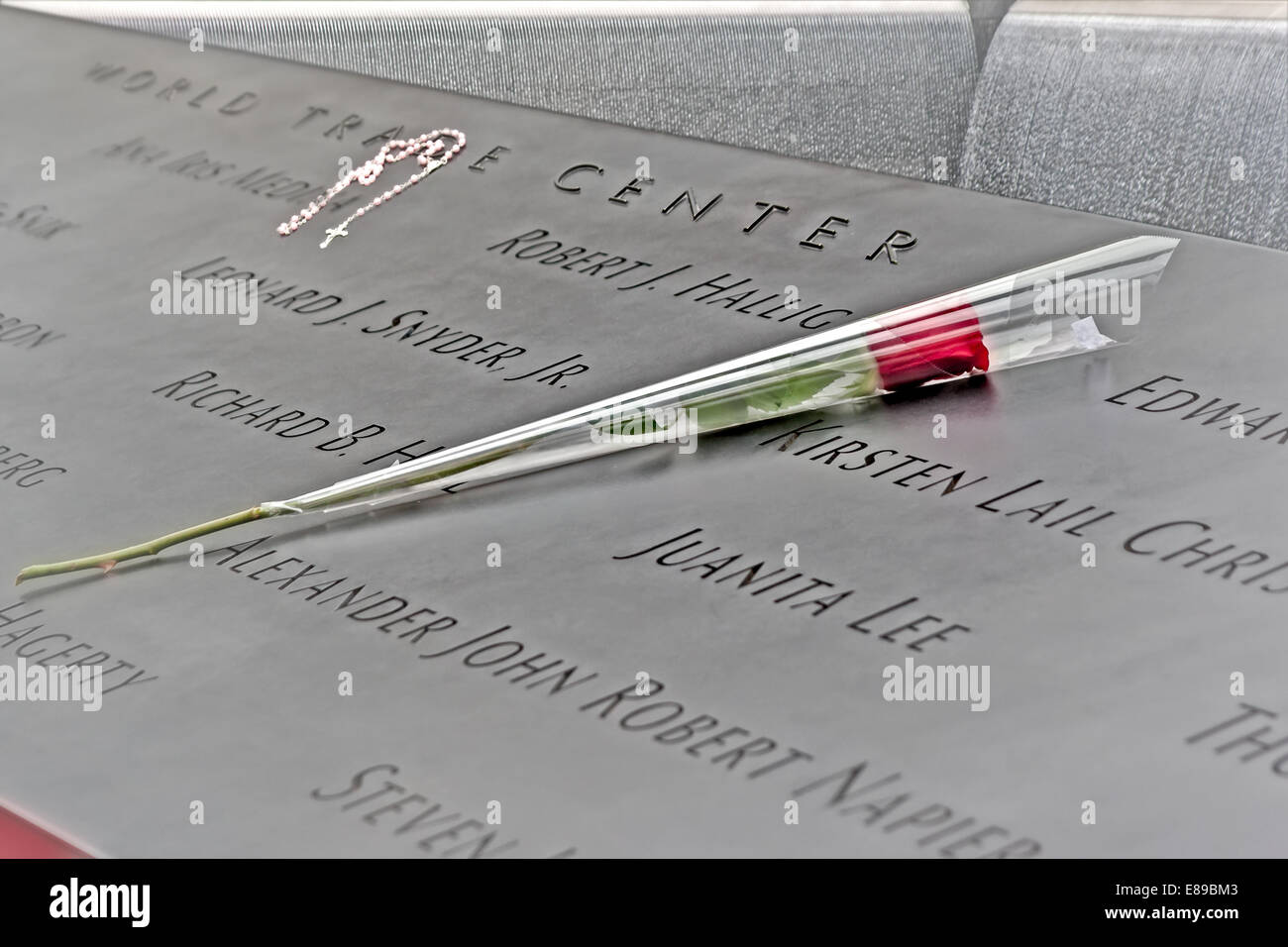 A red rose and a rosary are left on top of the engraved names of the victims of the September 11th terrorist attacks.  A view to the water falling into the pools at the World Trade Center Memorial in New York City can be seen in the top. Stock Photo