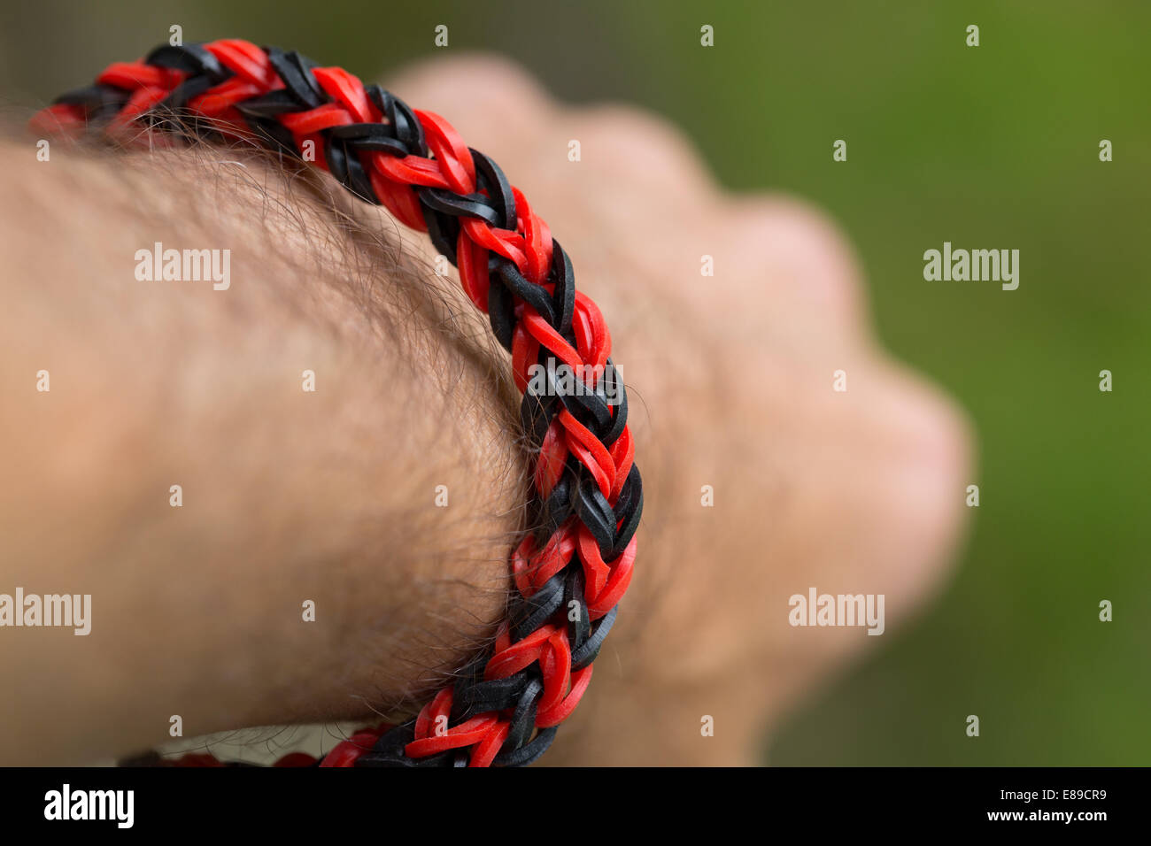 A red and black bracelet made from loom bands on a man's wrist. Model Released. Stock Photo