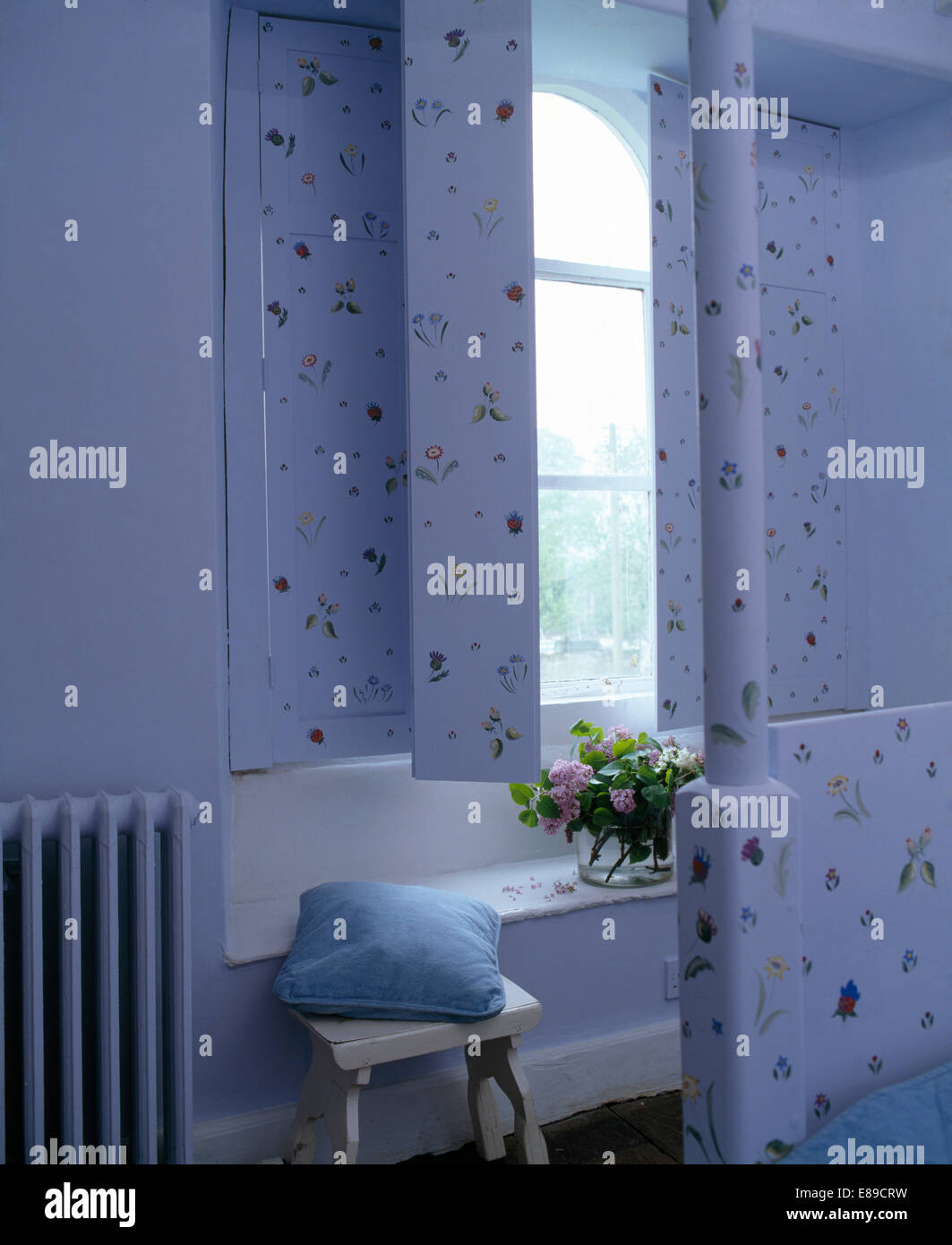 Pale blue painted shutters with floral decoration on window in pale blue country bedroom Stock Photo