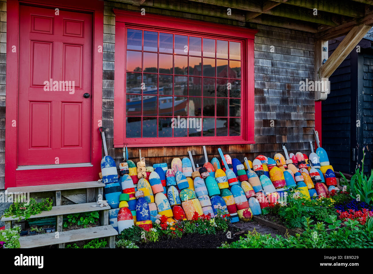 Rows of colorful buoys lined up in a storefront with Motif Number One reflected in the window panes. Bradley Wharf in Rockport, Massachusetts. Stock Photo