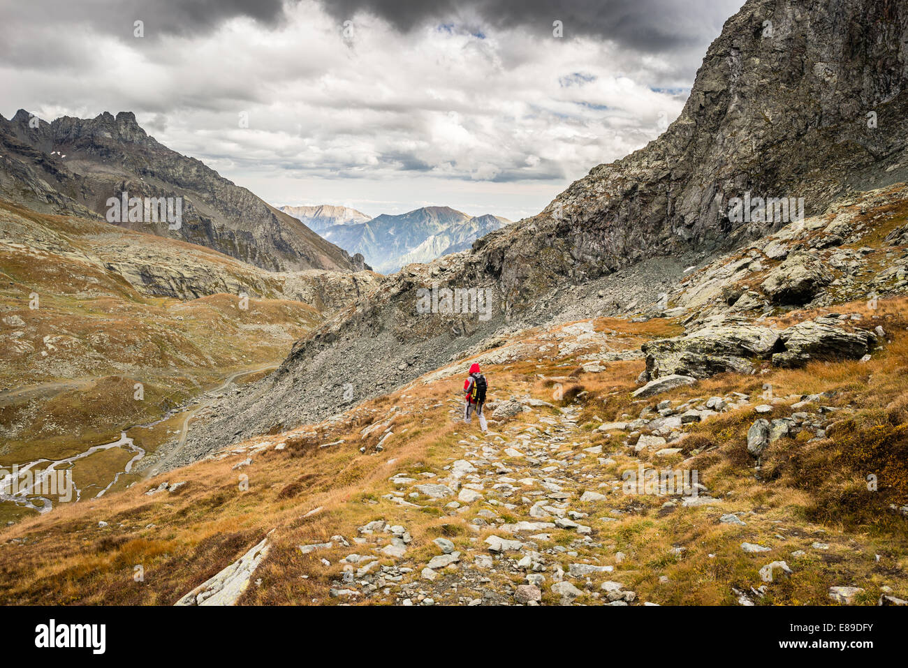 Hiker walking on dangerous footpath crossing a steep rocky slope with great panoramic view and dramatic sky. Stock Photo