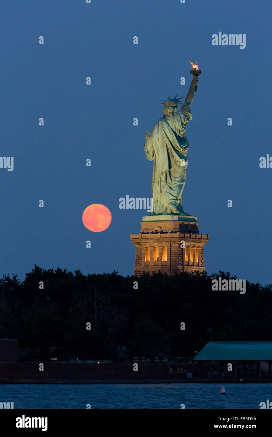 The super moon rises next to the Statue of Liberty during twilight. Stock Photo