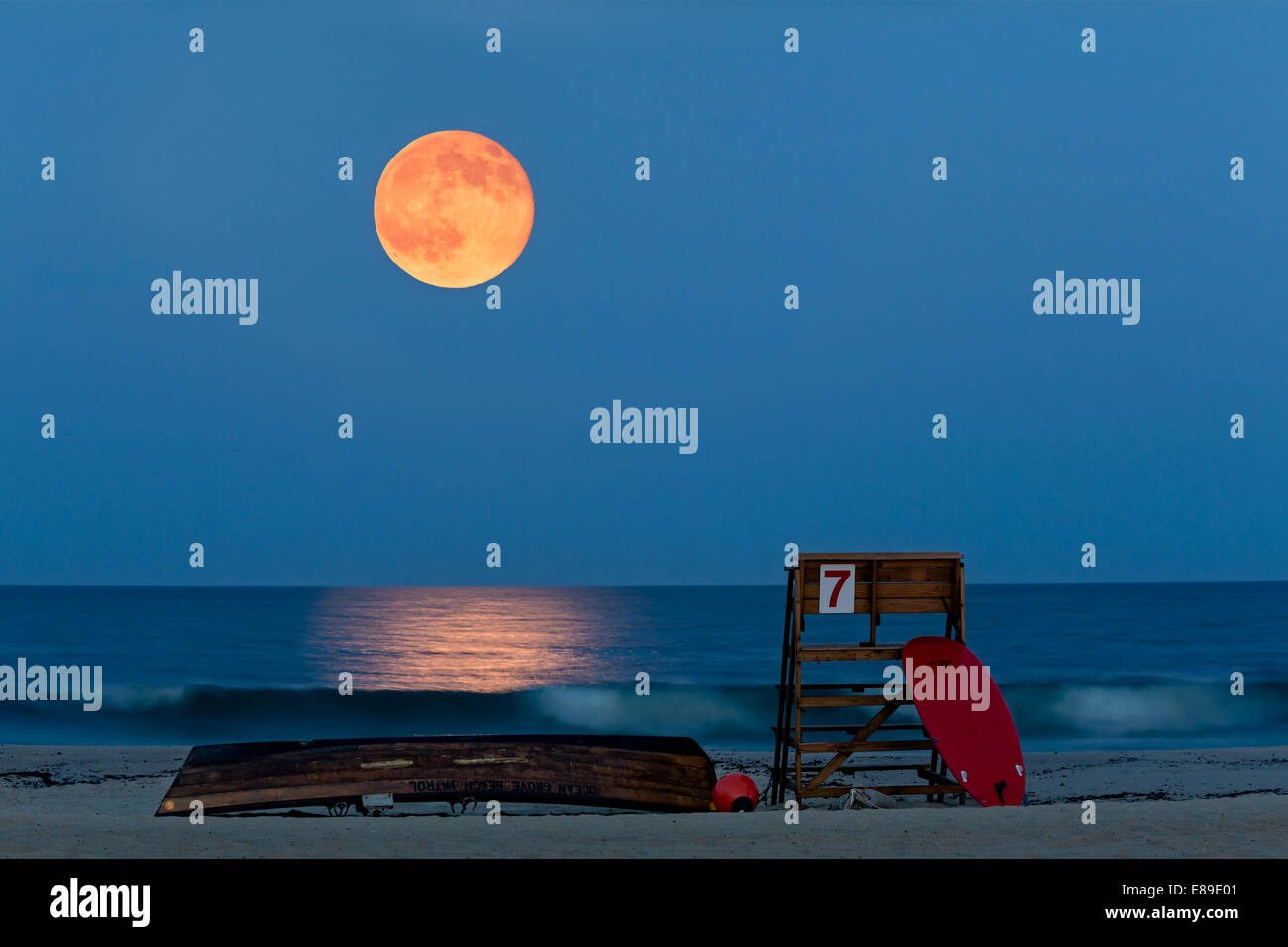 Super moon rising during twilight over Asbury Park Beach, New Jersey, with life guard stand, Ocean Grove Beach Patrol canoe and surf board as the foreground. Stock Photo