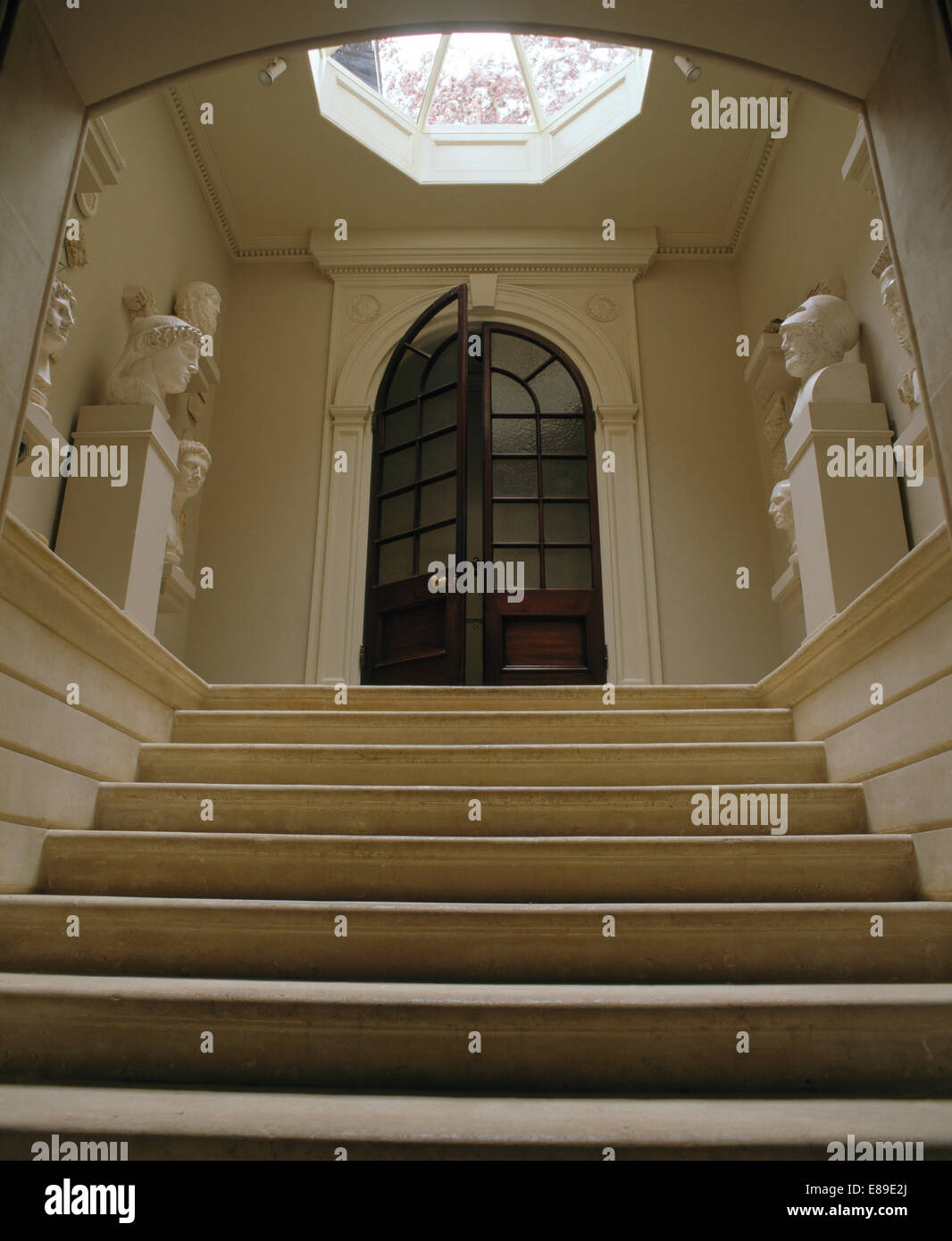 Stone staircase and busts on plinths in large hall with half glazed double doors Stock Photo