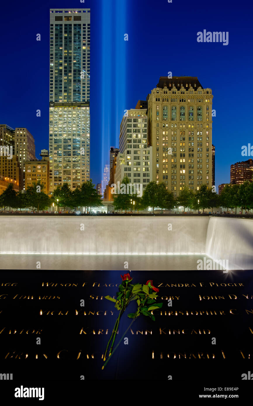 Ground Zero - 911 Tribute In Lights Memorial from Ground Zero with one of the two reflecting pools and the two beams of lights shinning high into the blue sky during twilight. All of the names of the victims from the September 11, 2001 and 1993 terror attacks are inscribed around the reflecting pools. The red roses where placed on the bronze panel edging the pool as a sign of remembrance. We will never forgot! Stock Photo