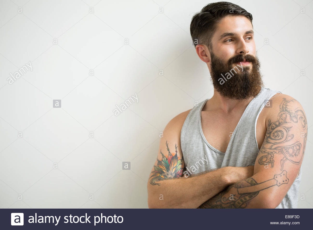 Bearded man with tattoos standing with arms crossed Stock Photo