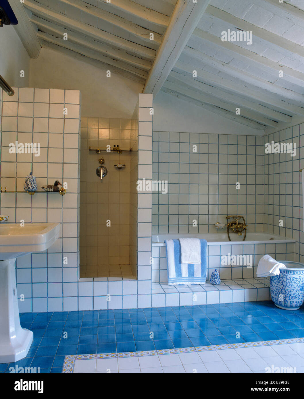 Aquamarine blue tiled floor in modern white tiled Tuscan bathroom with white painted ceiling beams Stock Photo