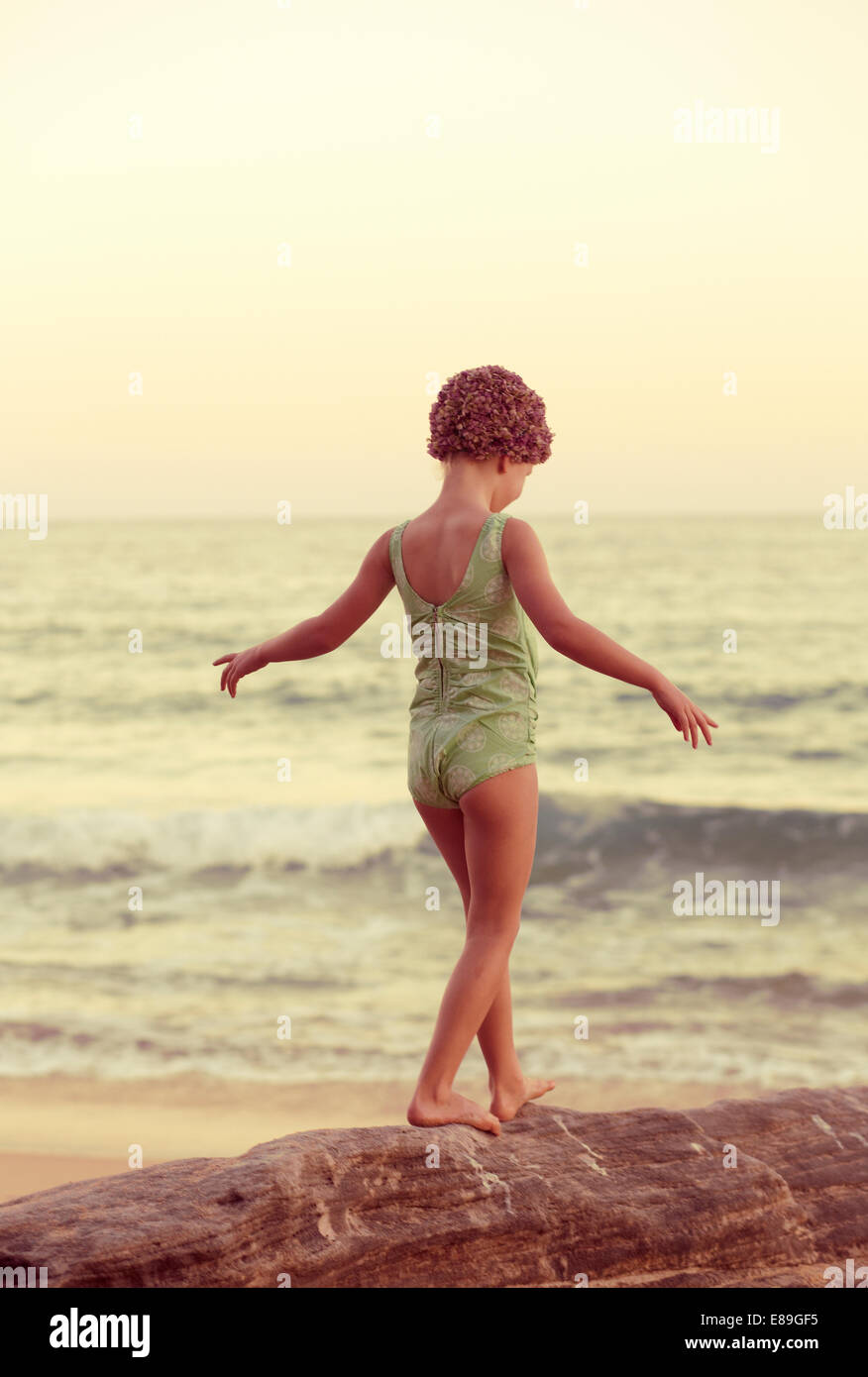 Girl in swimcap walking along oceanside rocks Stock Photo