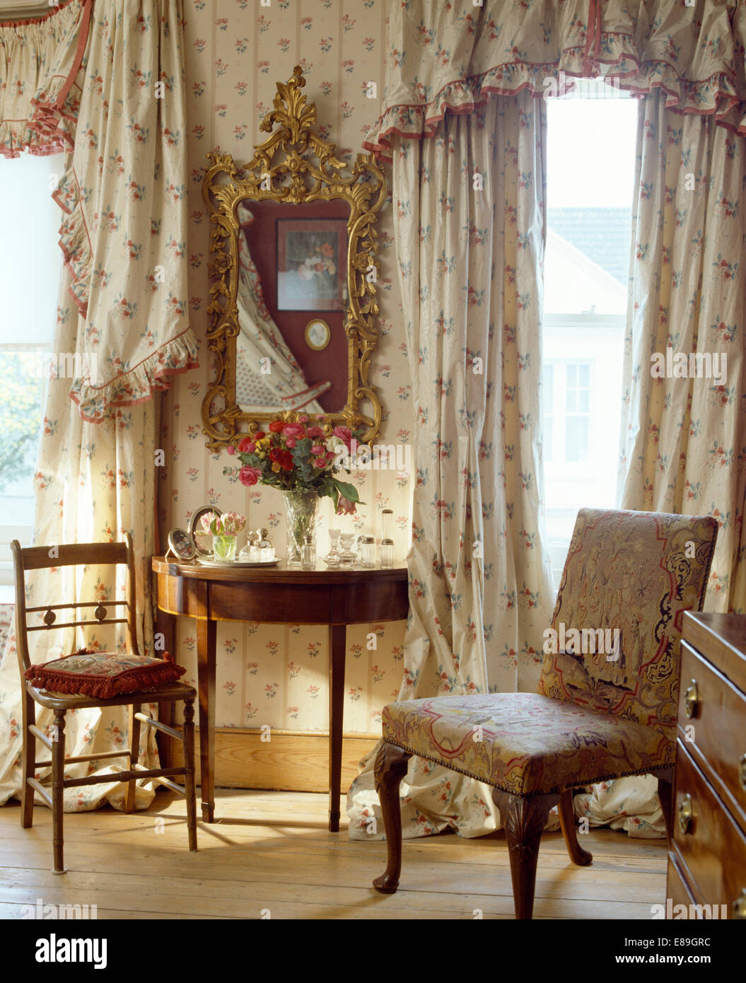 Floral curtains and pelmet on windows in bedroom with antique gilt mirror above antique console table Stock Photo