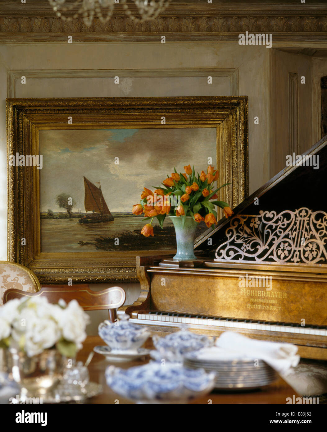 Close-up of piano with vase of orange tulips on piano in country dining room with old oil painting on the wall Stock Photo
