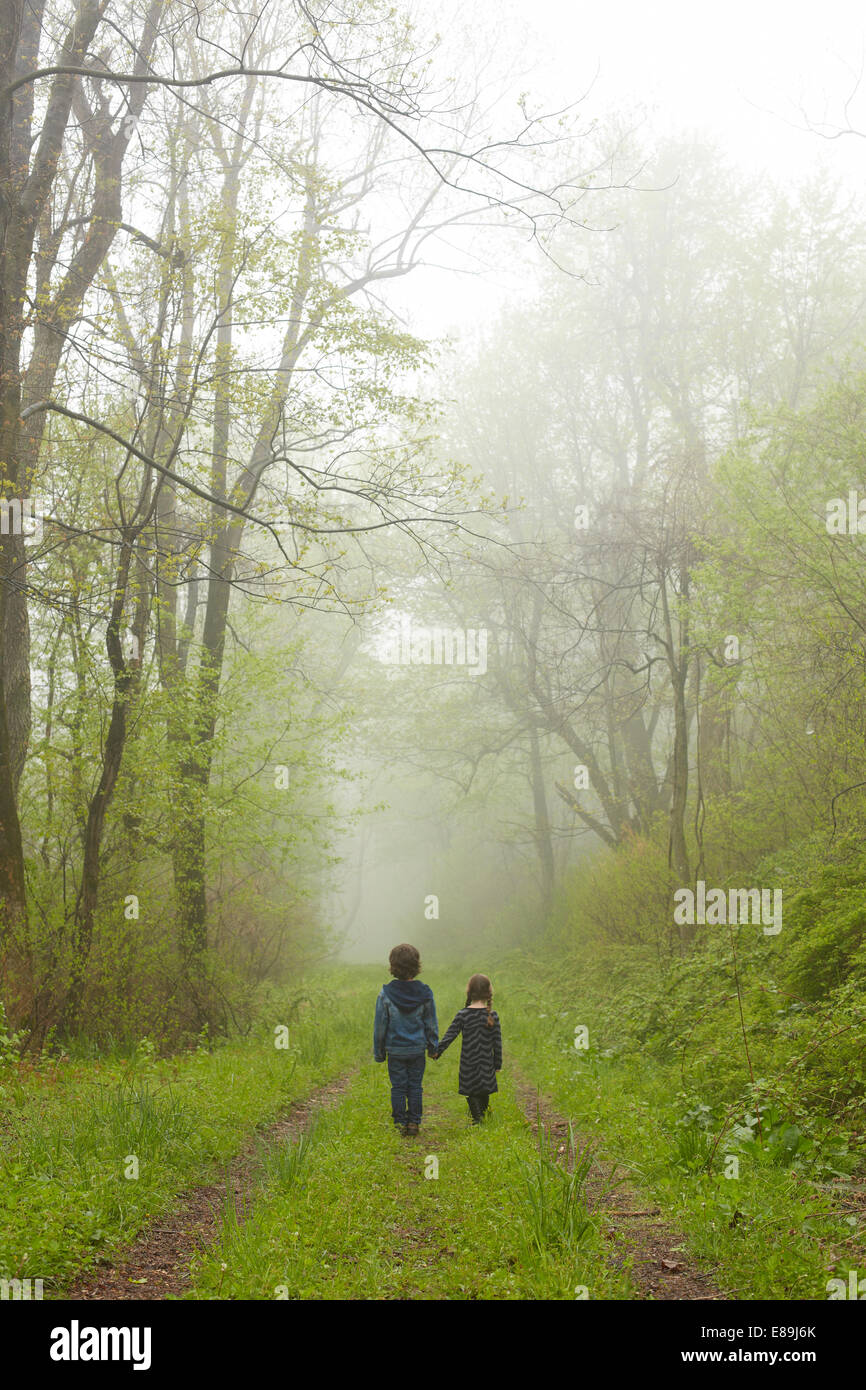 Brother and sister walking down foggy path Stock Photo