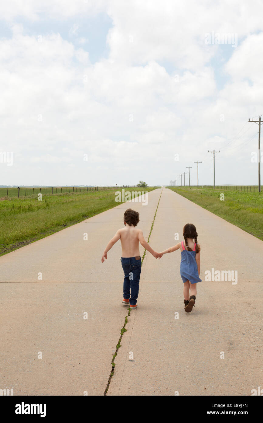 Brother and sister walking along sidewalk in country Stock Photo - Alamy