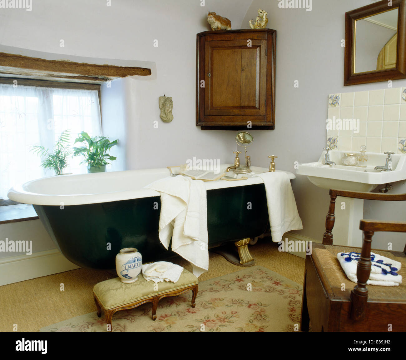 Antique corner cupboard on wall above roll top bath in white country