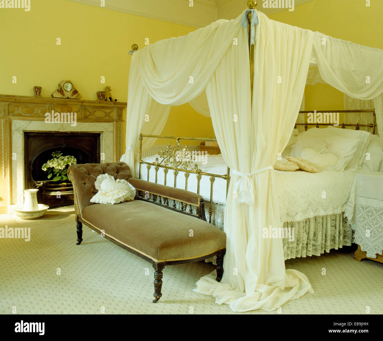 White voile drapes on fourposter bed in yellow bedroom with velvet