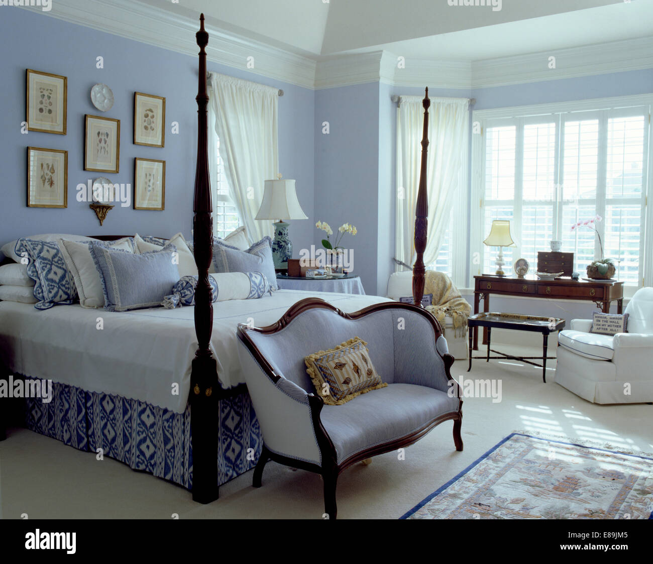 Pale blue sofa below bed with turned spindles and blue+white cushions in pale blue coastal bedroom Stock Photo