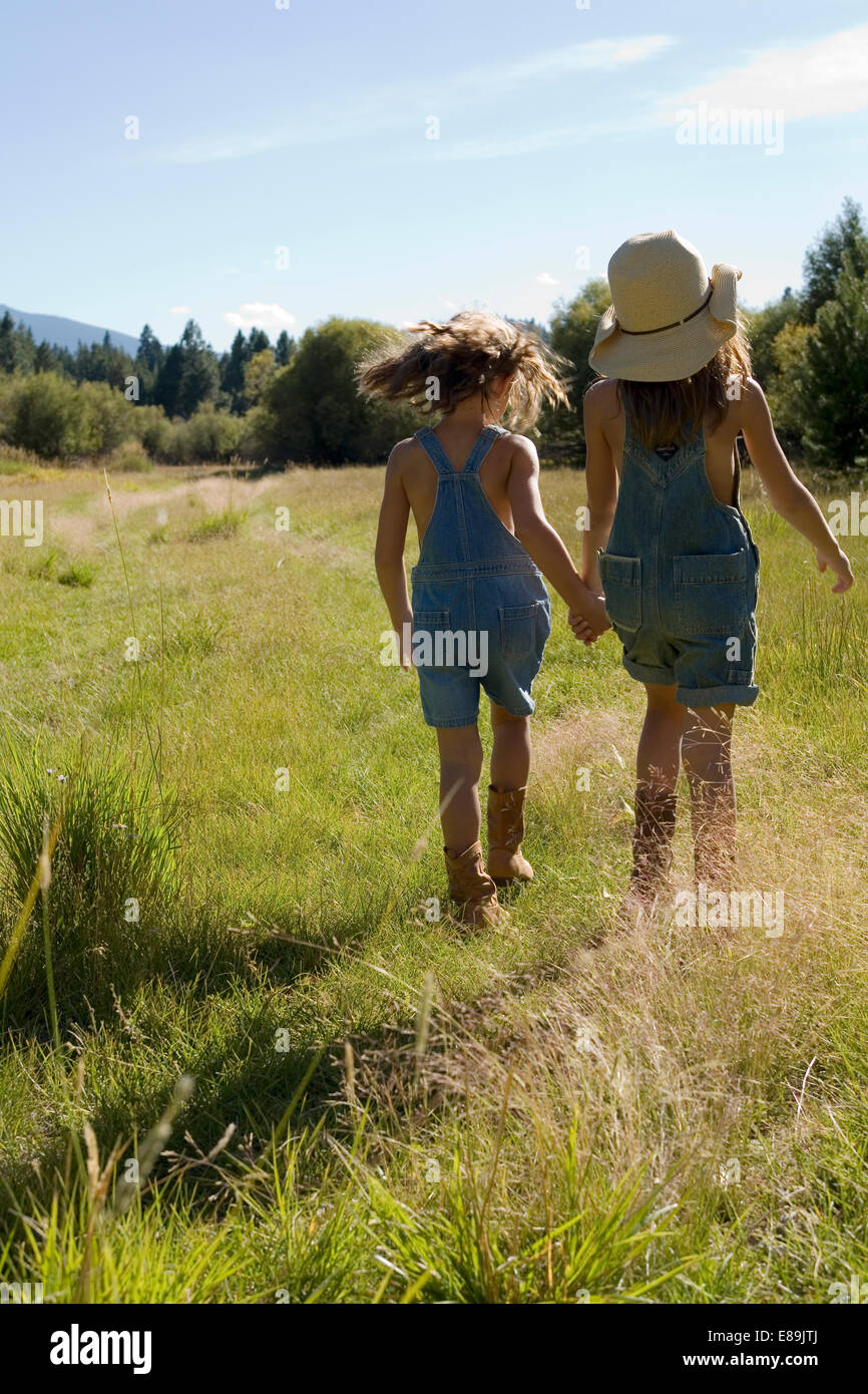 Sisters in overalls walking in field Stock Photo