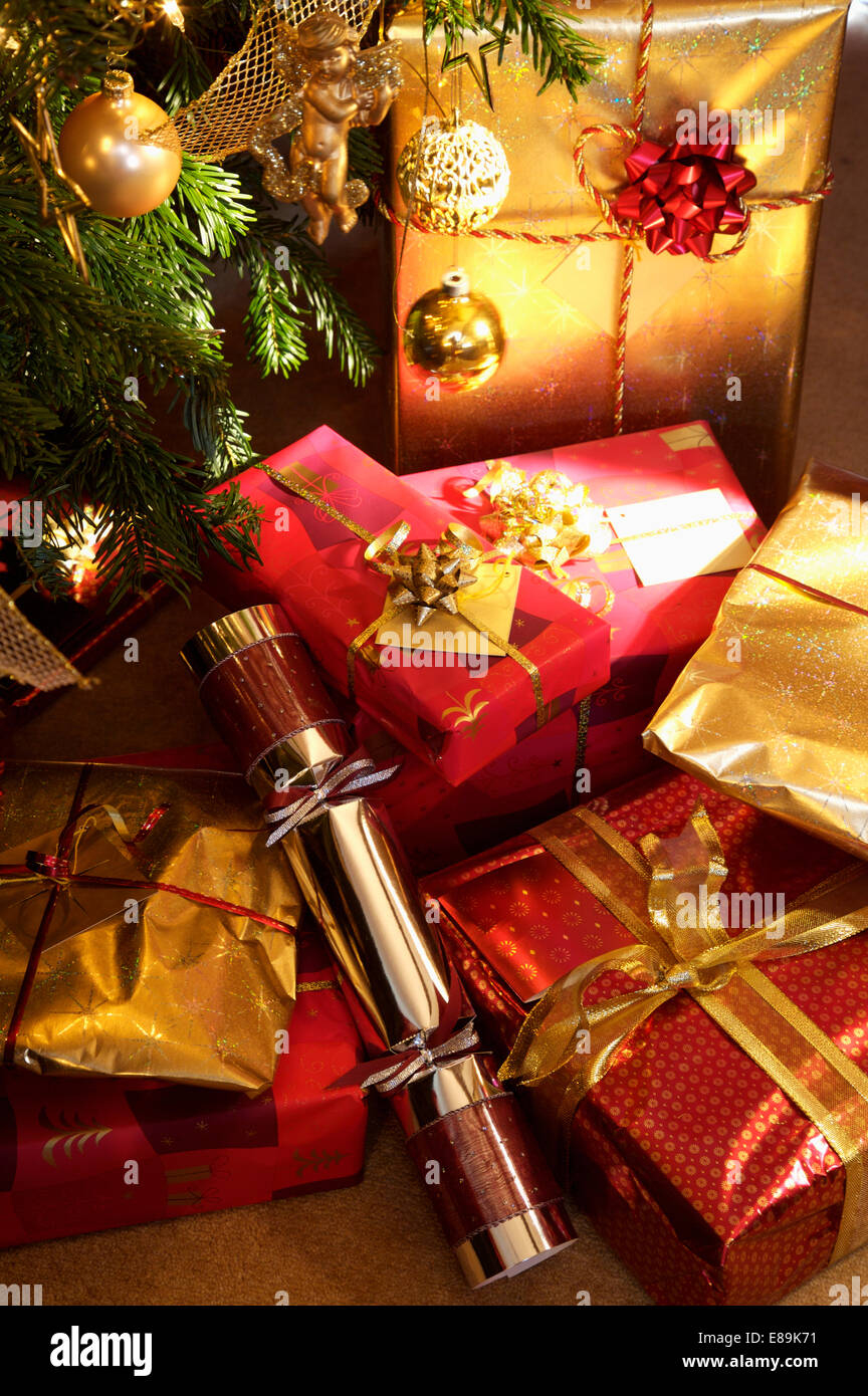Close-up of metallic gold and red wrapped Christmas gifts below tree Stock Photo