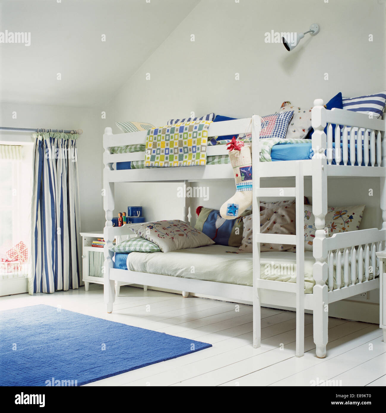 Christmas stocking on white bunk beds piled with cushions in children's white attic bedroom with blue rug on white floor Stock Photo