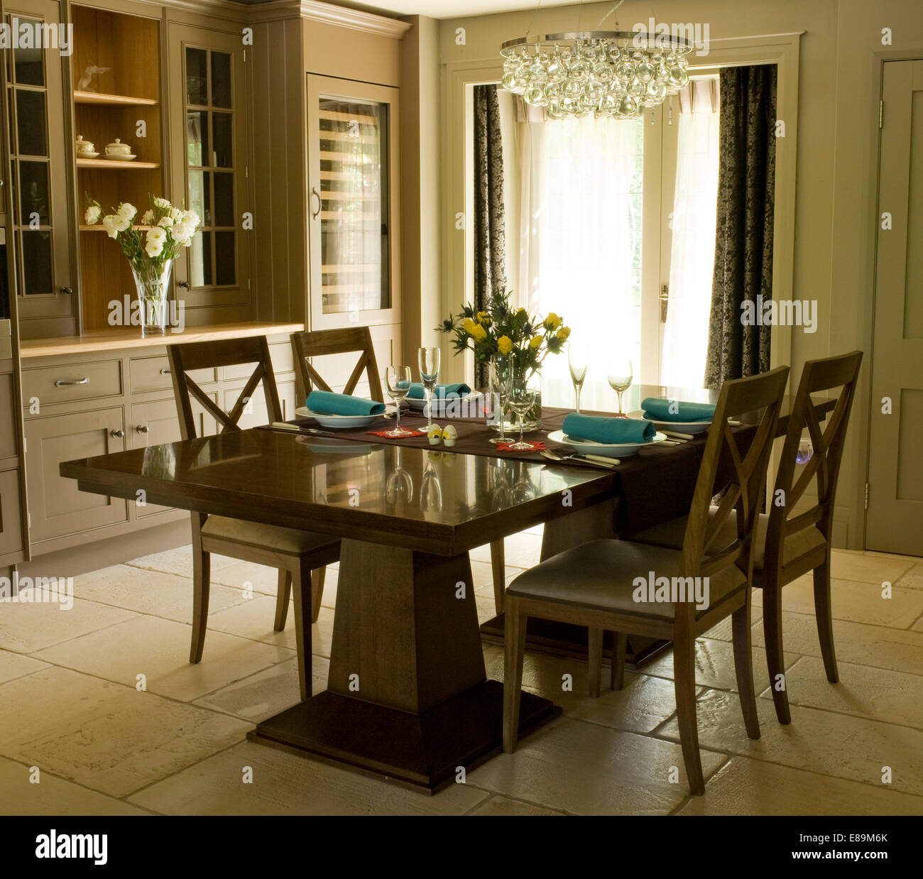 Glass light fitting above rectangular table and painted chairs in centre of modern dining room Stock Photo