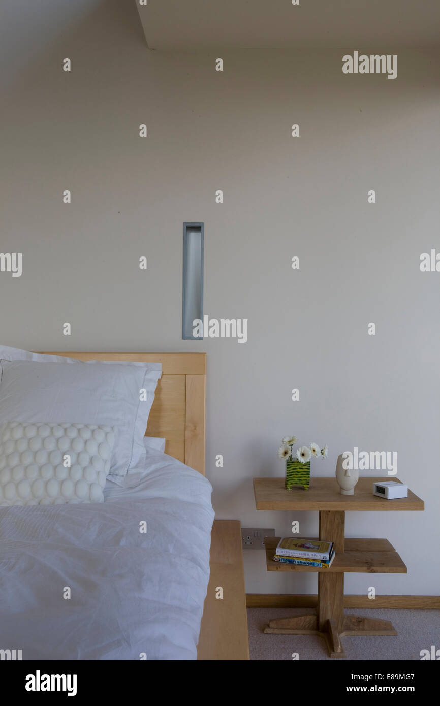 Simple wooden table with integral shelves beside bed in modern bedroom