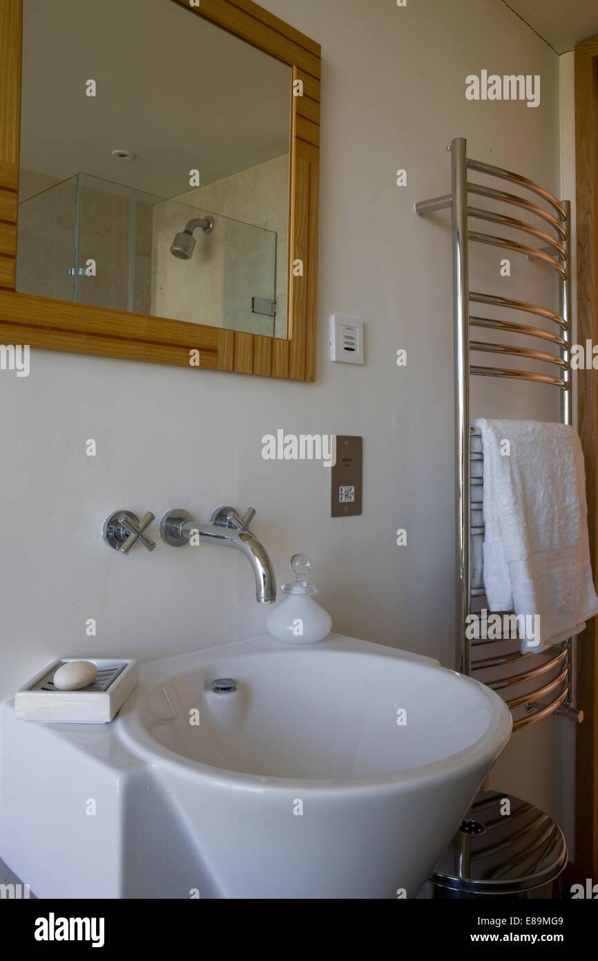 Mirror above wall mounted tap fitting over washbasin in modern bathroom with chrome towel rail Stock Photo