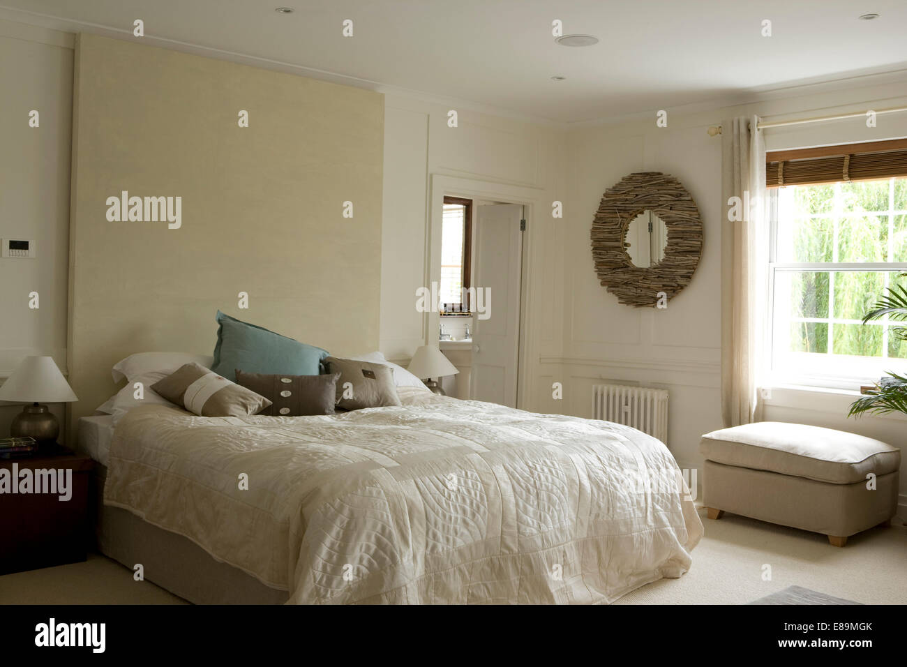Double bed with headboard panel and white quilt in light and airy bedroom Stock Photo