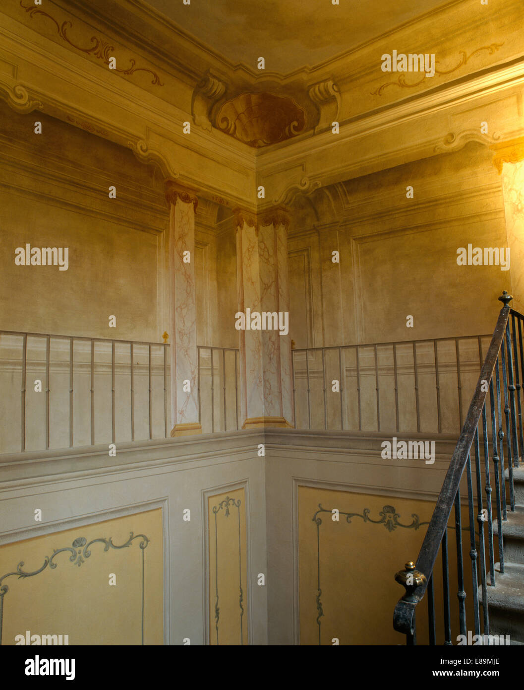 Trompe l'oeil painted walls in large Tuscan hall with metal banisters on staircase Stock Photo
