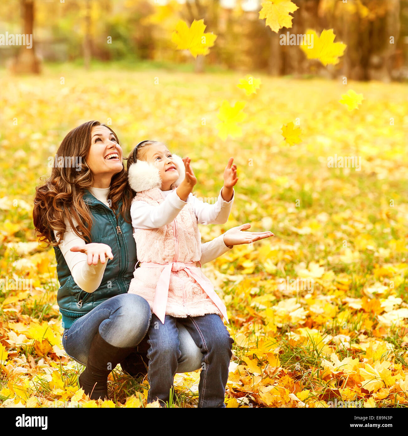 Mother and daughter having fun in the autumn park among the falling ...