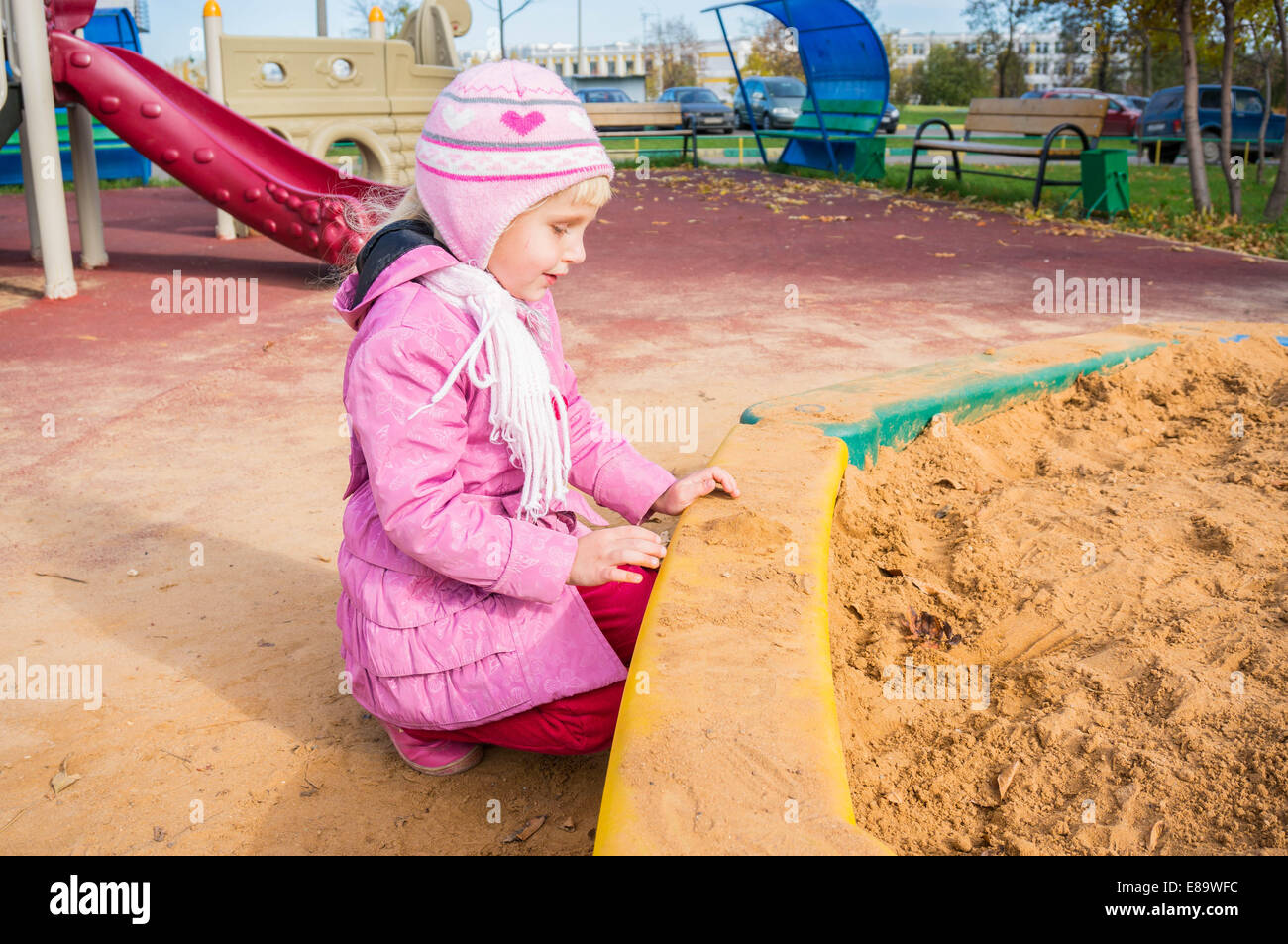 sad girl on the empty sandpit playground in autumn Stock Photo