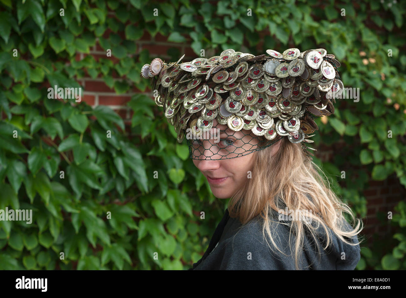 Young woman wearing a hat made of crown corks in front of a wall of leaves, Germany Stock Photo