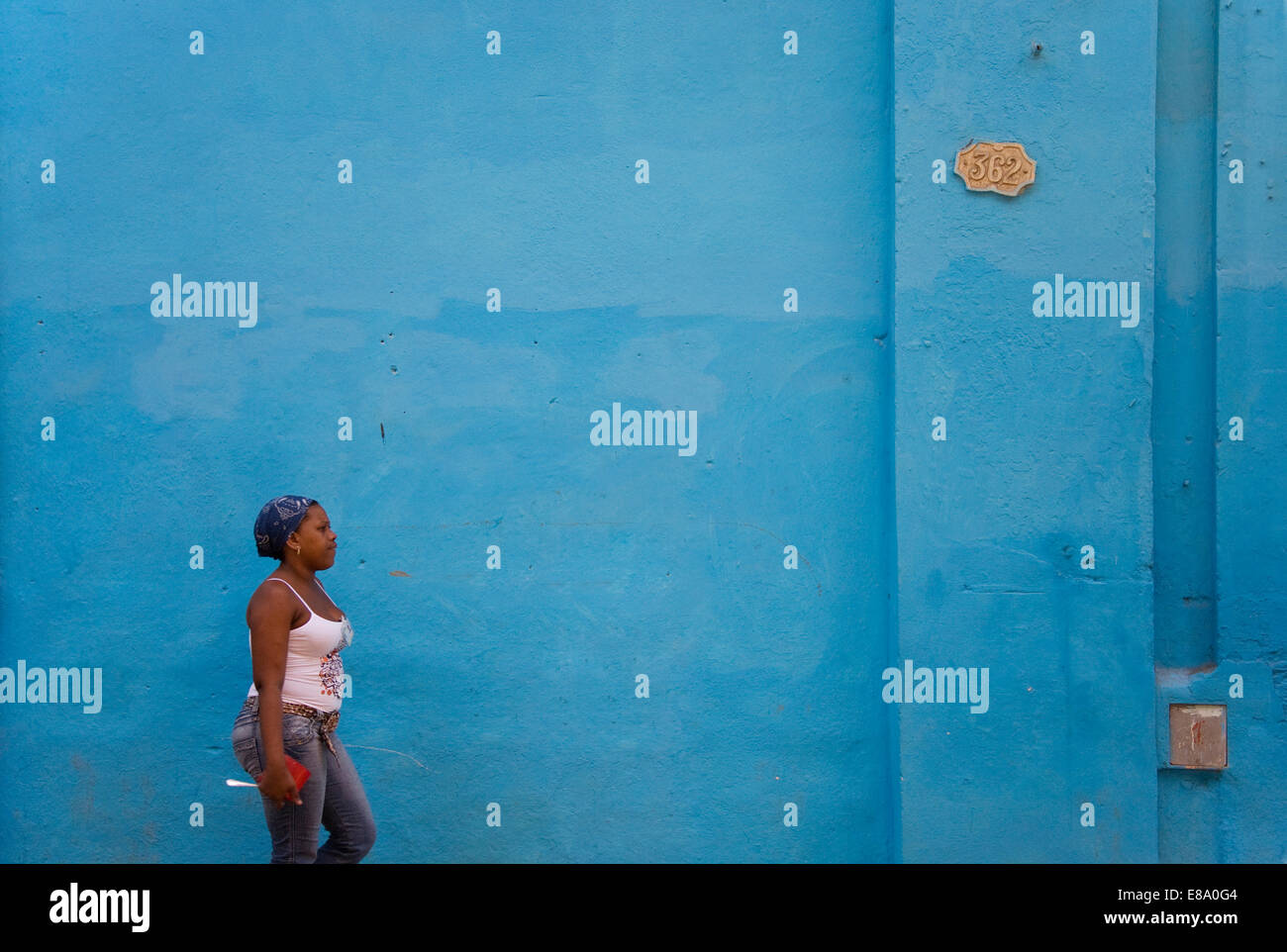 Local woman walking past a blue wall, Old Havana, Havana, Cuba Stock Photo