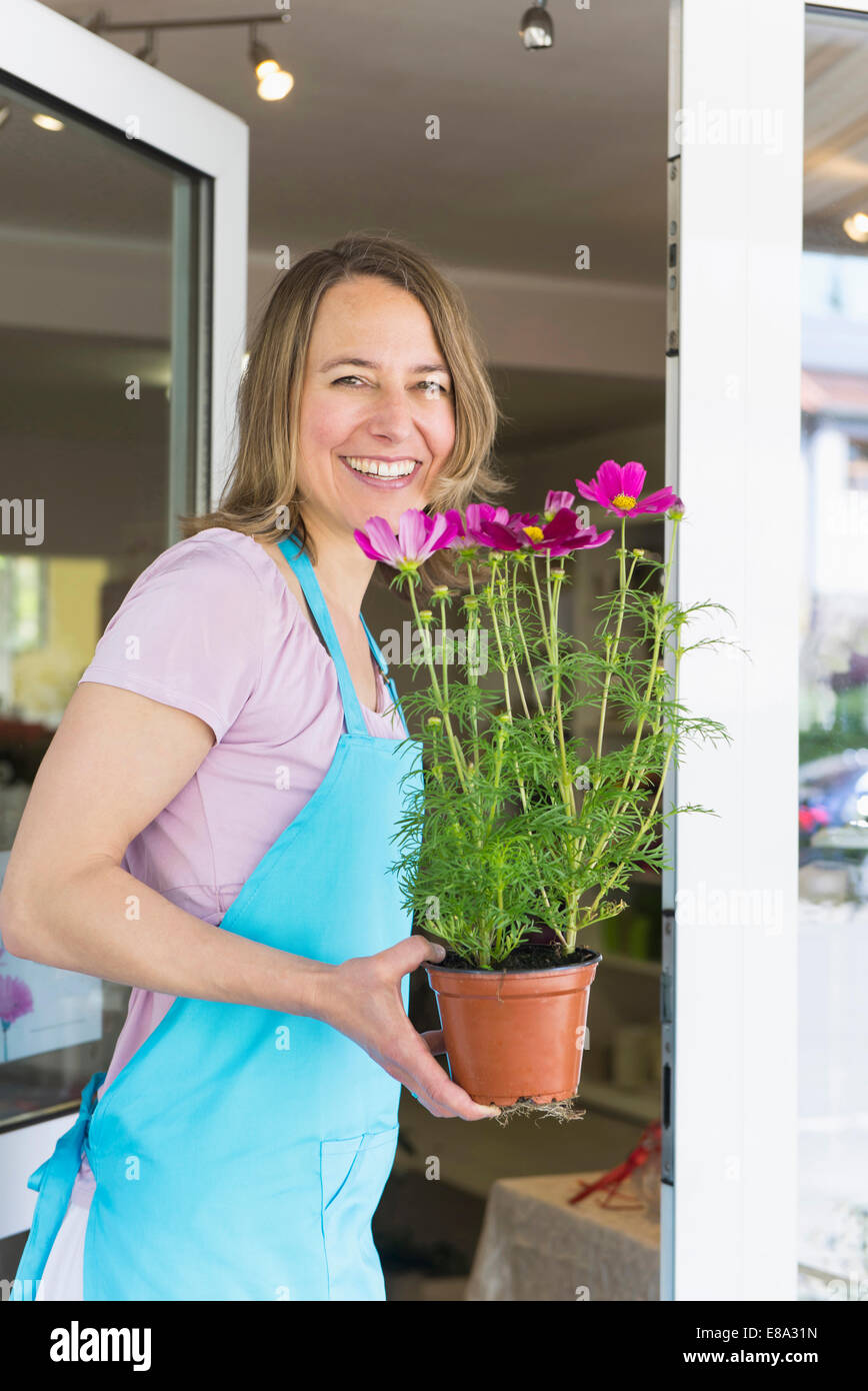 Portrait of mid adult woman holding potted plant of flower, smiling ...