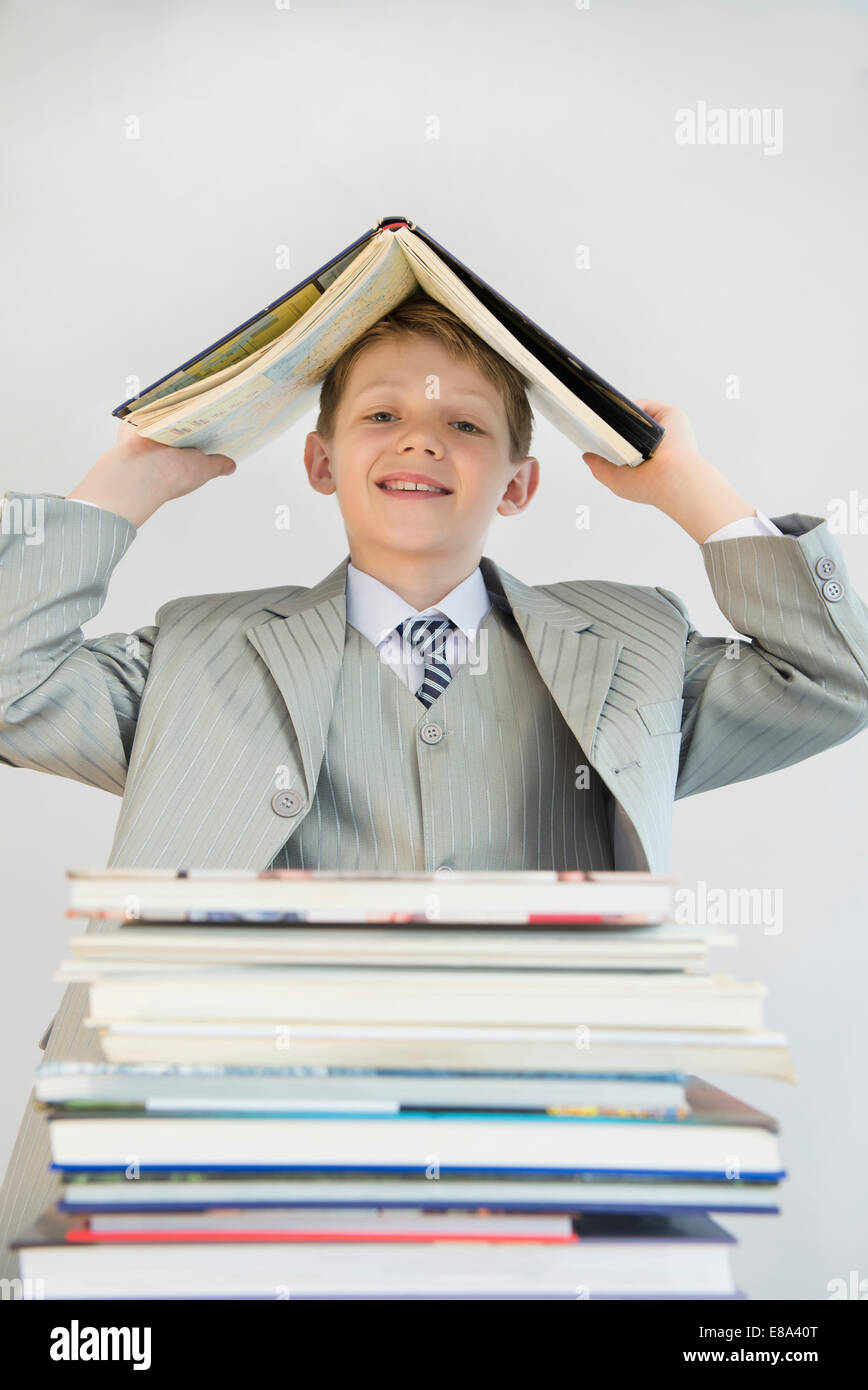 Portrait of boy with stack books, holding one book over his head as roof Stock Photo